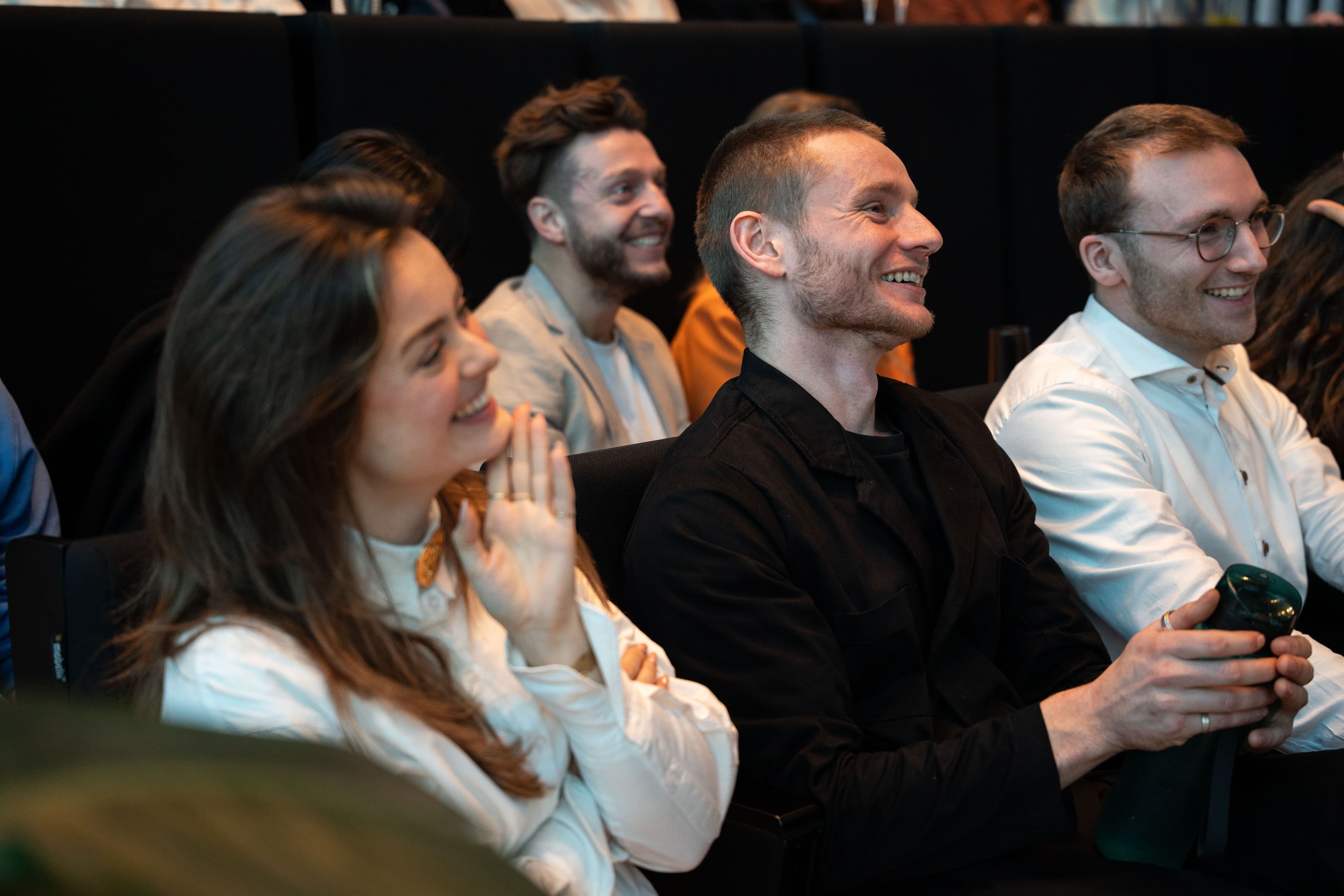 A smiling woman holding a Fritz cola in the atrium surrounded by a group of colleagues listening to her.